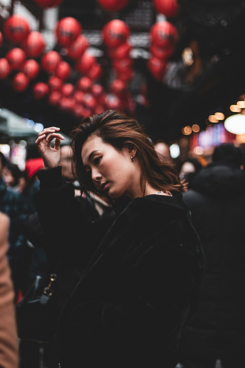 woman in black coat standing near red round fruits during nighttime