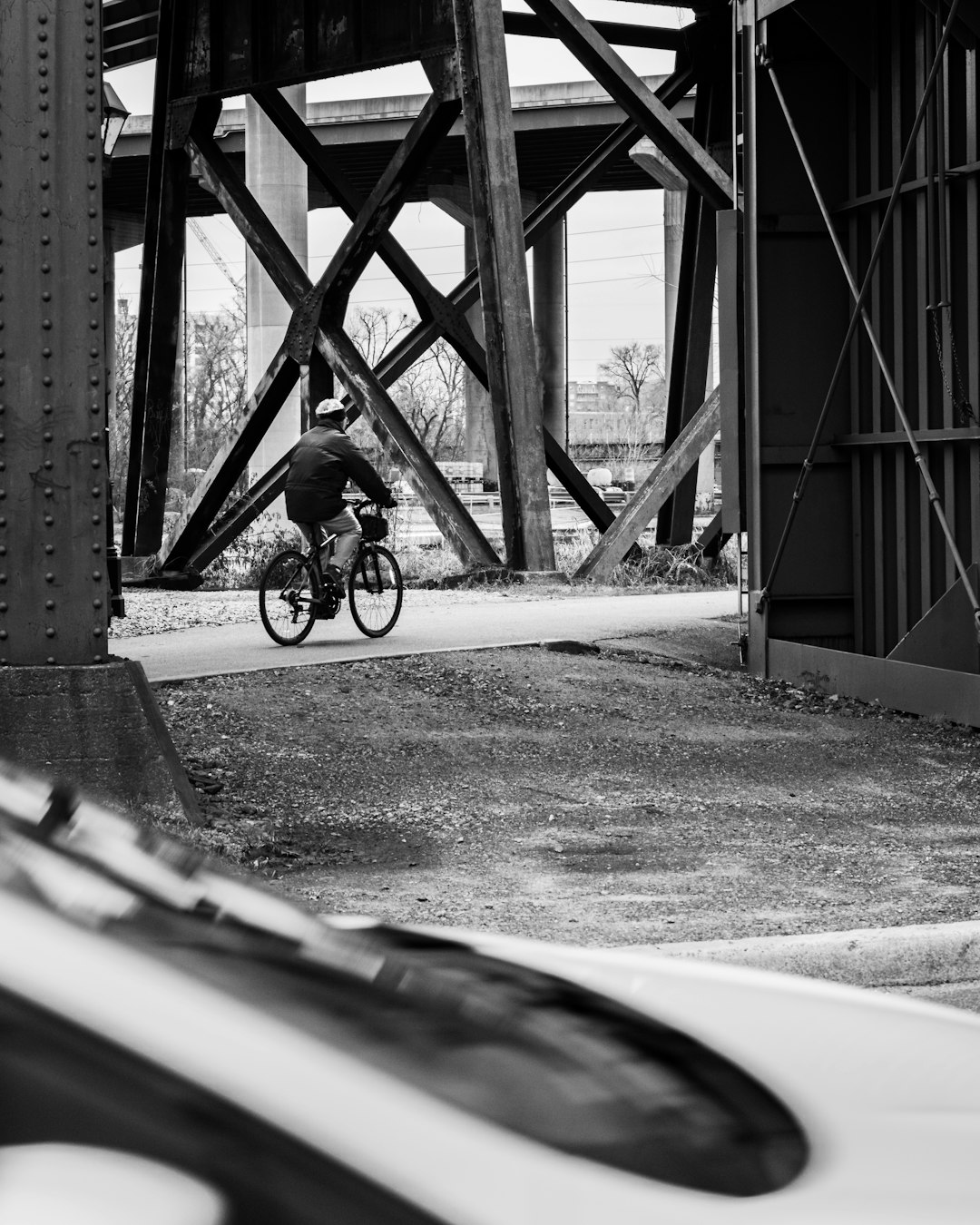grayscale photo of man riding bicycle on road near bridge
