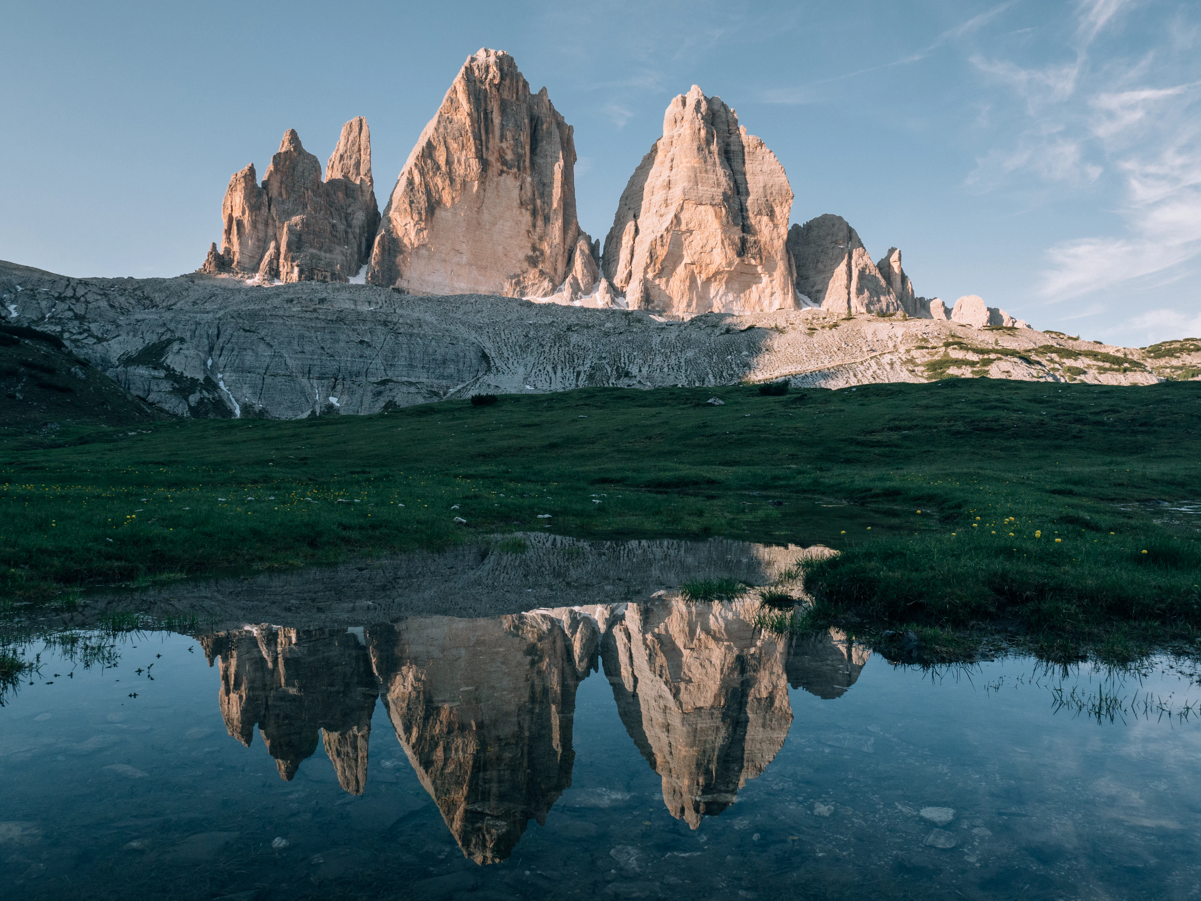 Tre Cime di Lavaredo uolų viršūnės virš žalių pievų ryto šviesoje, Dolomitai