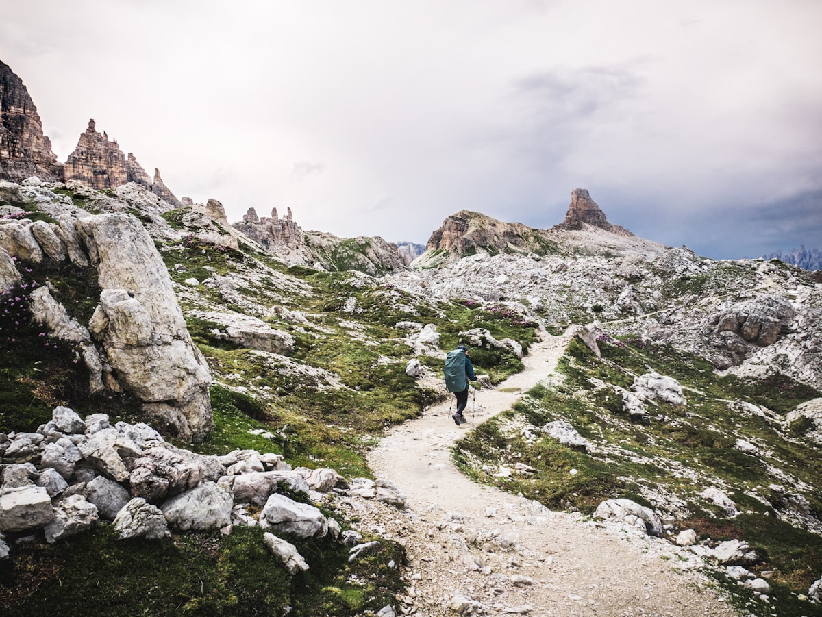 Person in blue jacket walking on gray rocky mountain during daytime