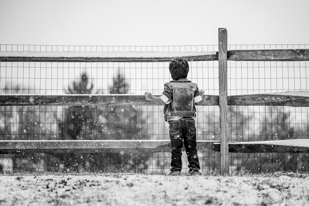Foto en escala de grises de un niño con chaqueta y pantalones de pie en el campo