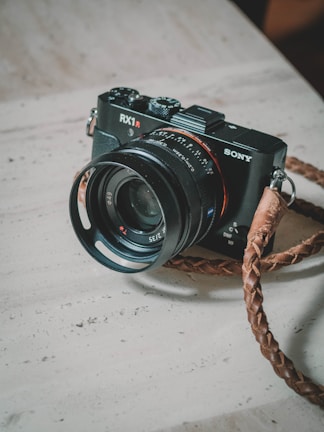Compact mirrorless camera placed next to a leather camera bag on a rustic surface.