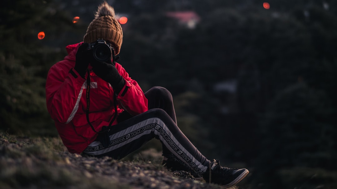 woman in red and black jacket and black pants sitting on rock