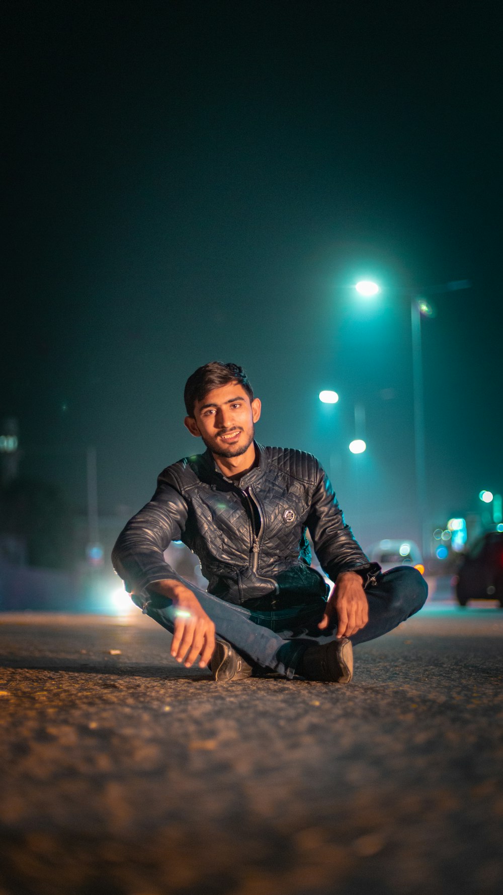 man in black leather jacket sitting on road during nighttime