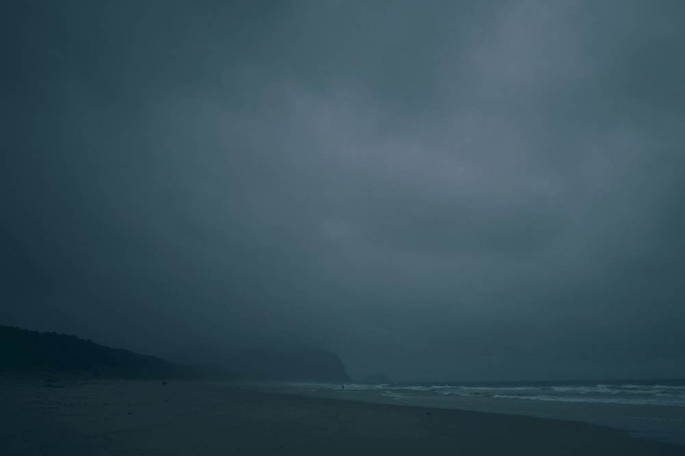 body of water near mountain under gray sky