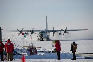 man in red jacket standing beside gray fighter plane