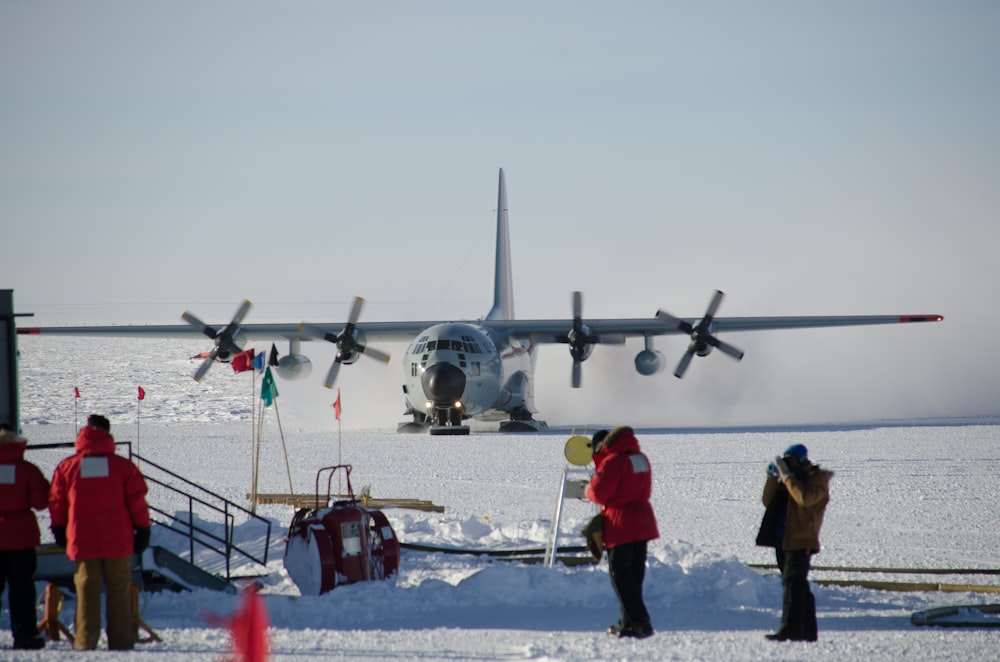 man in red jacket standing beside gray fighter plane