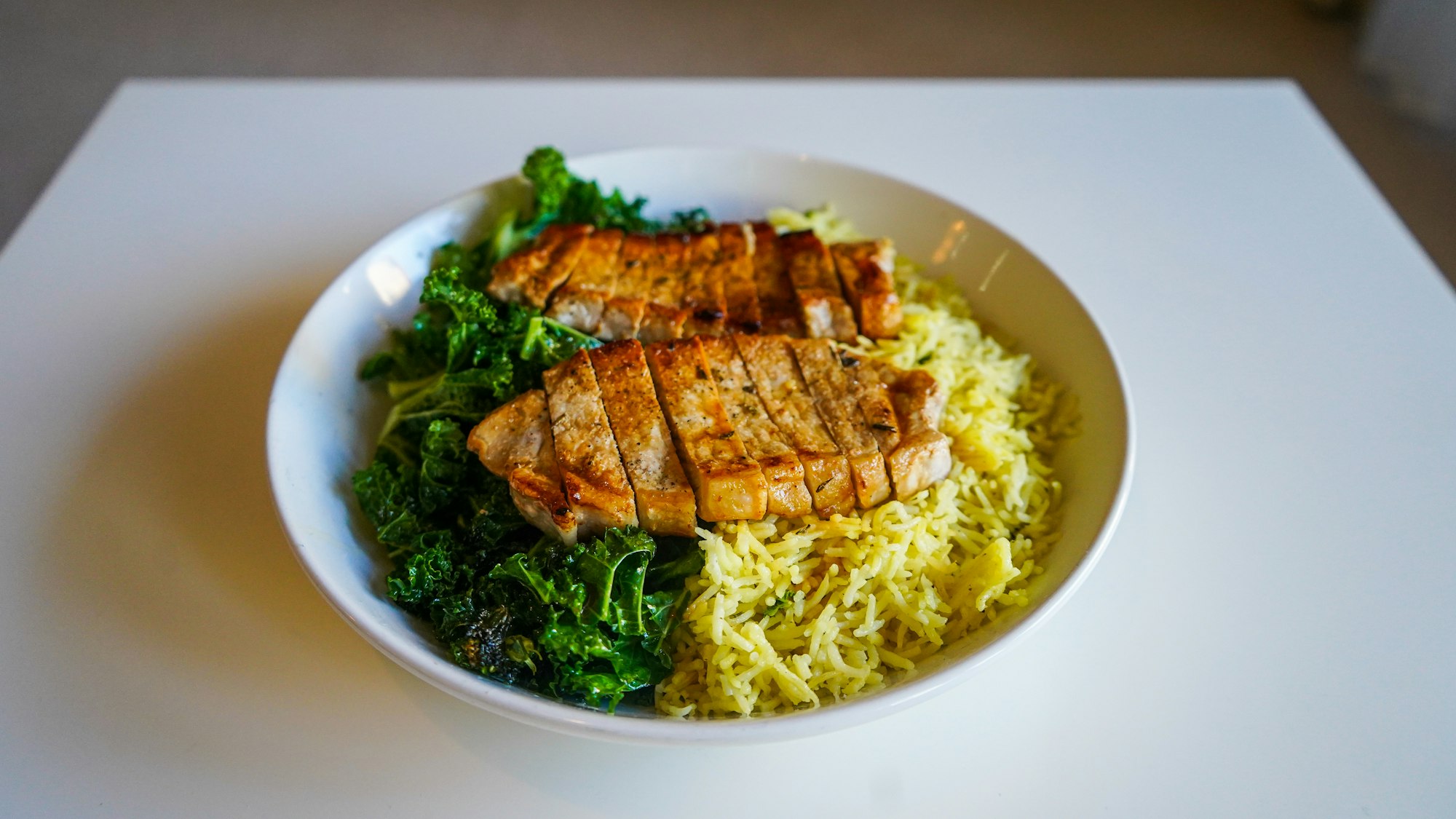 A freshly served bowl of Pork Loin Steaks on a bed of Kale and Lemon Rice.
