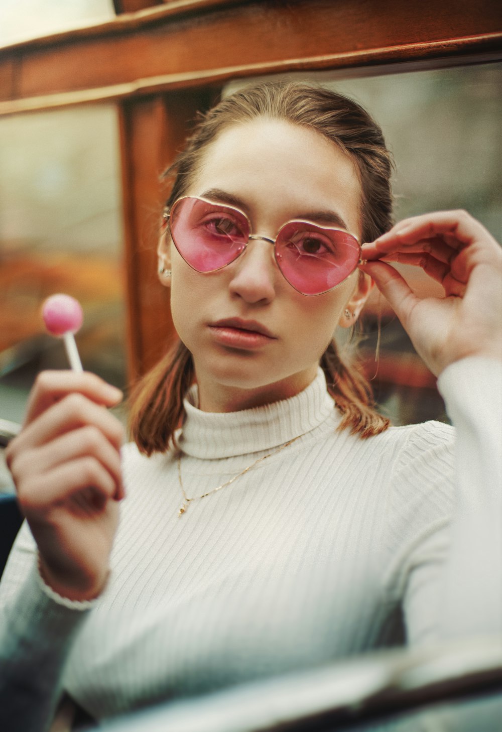 woman in white turtleneck sweater wearing red framed eyeglasses holding pink lollipop