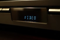 A close-up of a digital display on an electronic device showing the word 'VIDEO' in blue LED light. The device appears to be metallic and has a modern design.