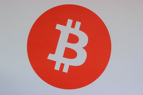 A bold orange circle dominates the center, featuring a prominent white Bitcoin logo, symbolizing cryptocurrency.