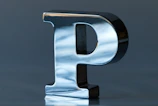 Side view of a large purple 3D printed letter 'J' with a matte finish on a wooden table.
