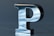A metallic 3D letter 'P' with a smooth, reflective surface catching light and shadow. It stands out against a soft blue-gray background, presenting a modern, sleek appearance.