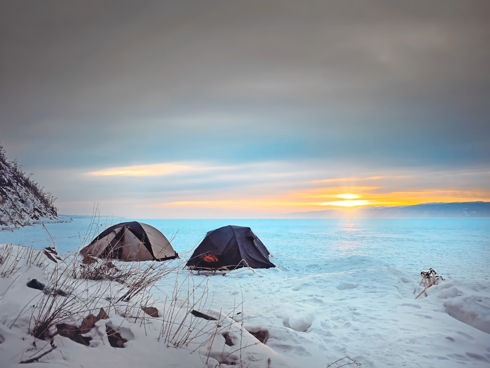 tenda preta no chão coberto de neve durante o pôr do sol