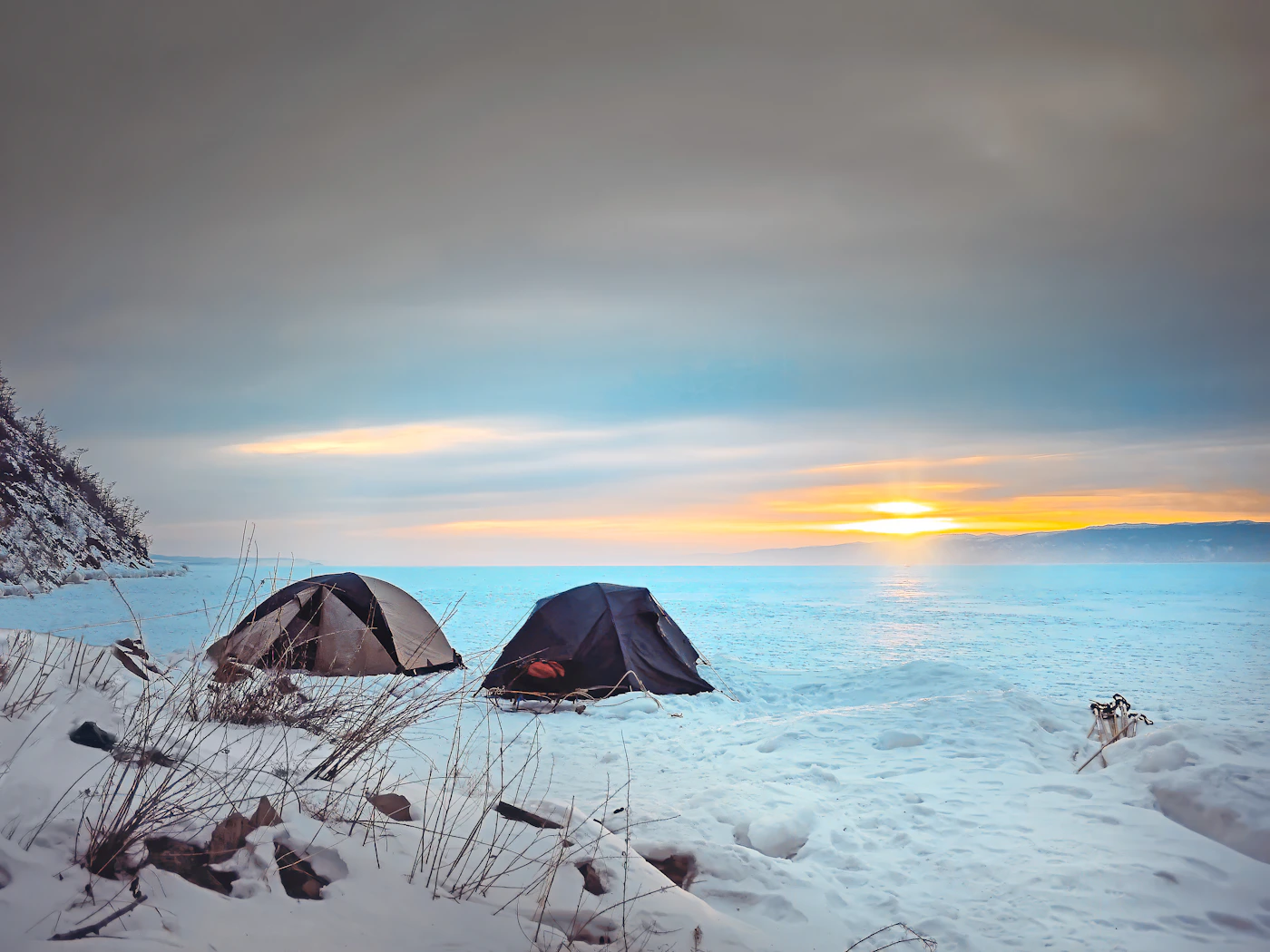 A distant tent silhouetted against a winter sunset over a frozen landscape