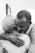 A heartfelt embrace between two people, one with short gray hair and the other with close-cropped hair. The setting appears intimate, suggesting comfort and warmth.