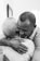 A heartfelt embrace between two people, one with short gray hair and the other with close-cropped hair. The setting appears intimate, suggesting comfort and warmth.