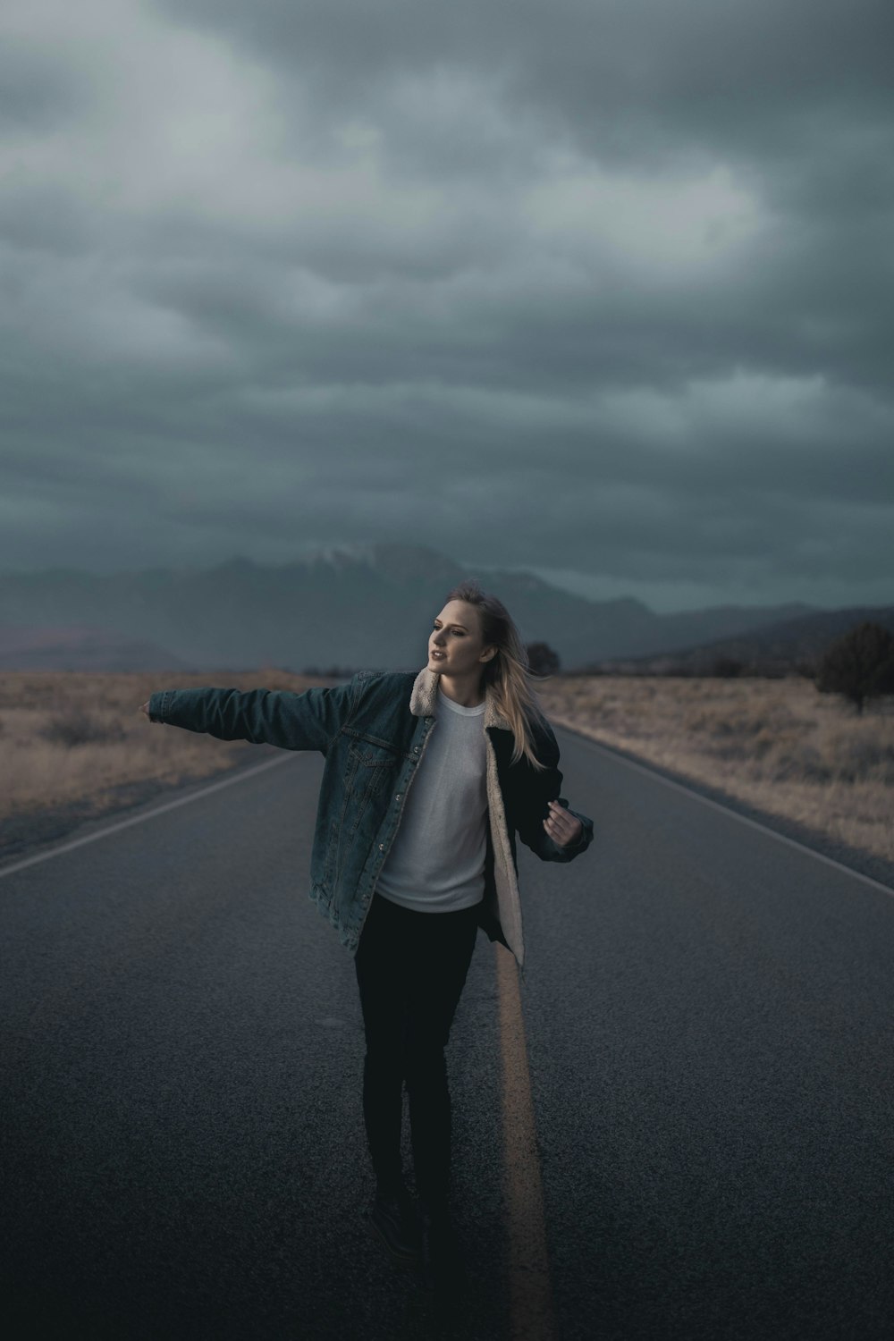 woman in gray jacket standing on road during daytime