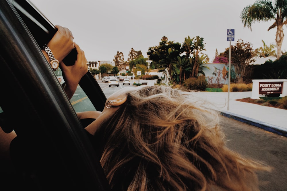 昼間、道路上の車の写真を撮る黒いジャケットの女性