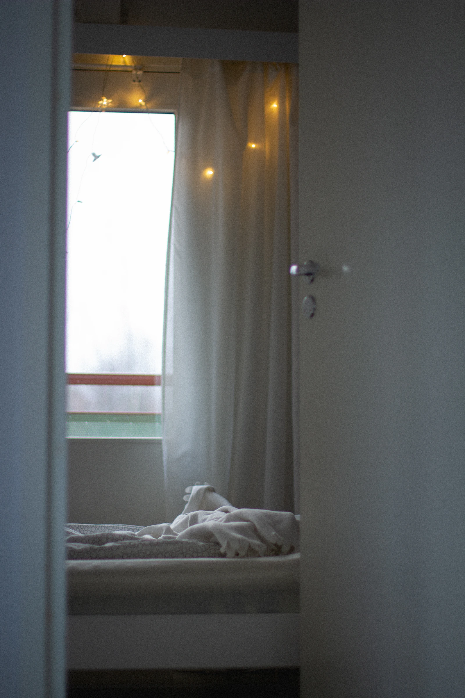 A simple bedroom with a white bed and white curtains by a window