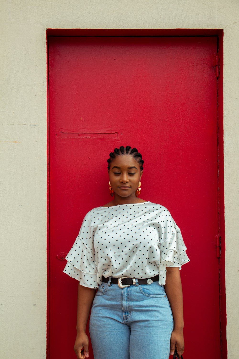 Muchacha con camisa blanca y roja de flores de pie junto a la pared roja