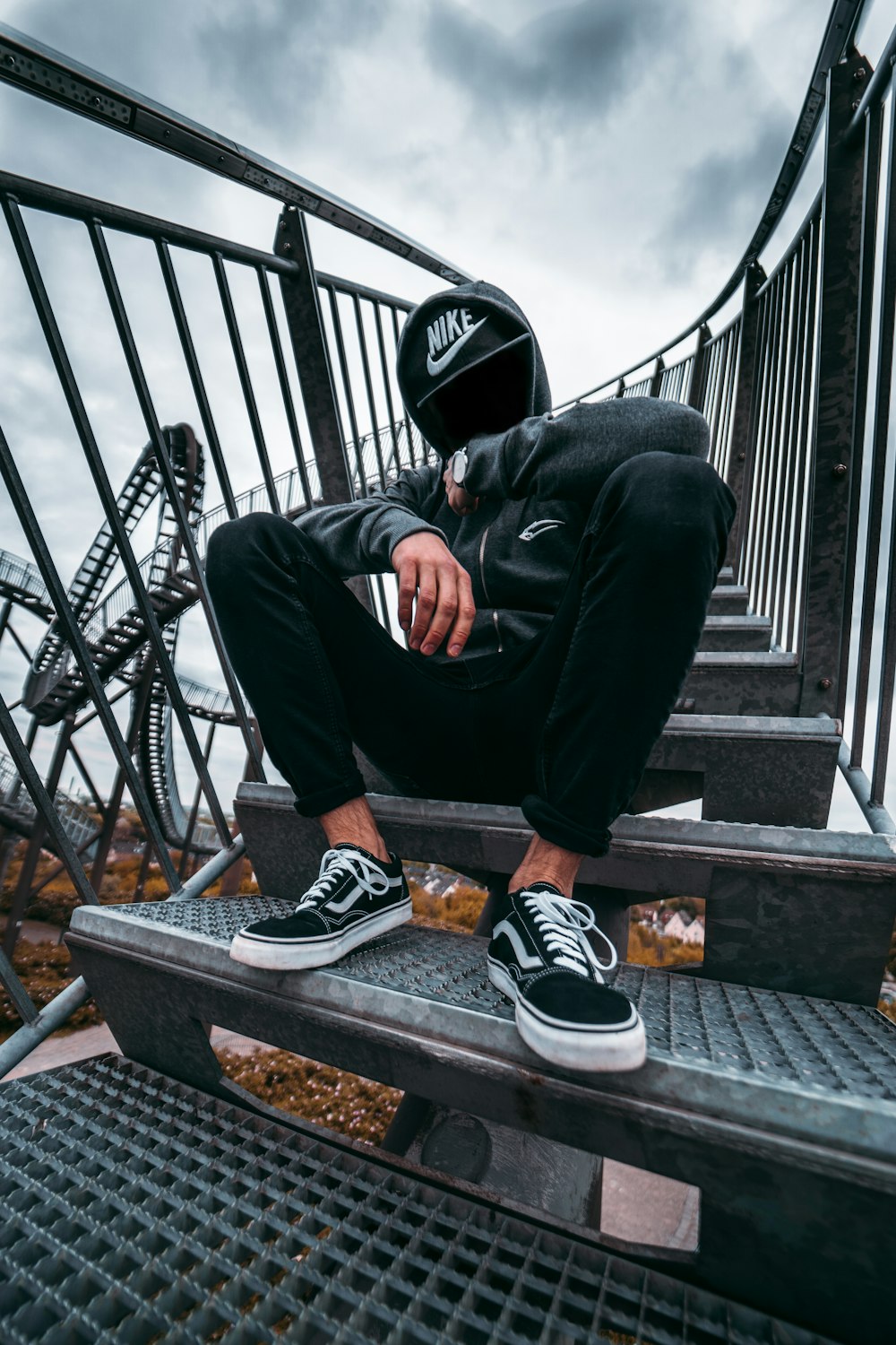 Hombre con pantalones negros y zapatillas Nike blancas y negras sentado en barandillas de metal negro