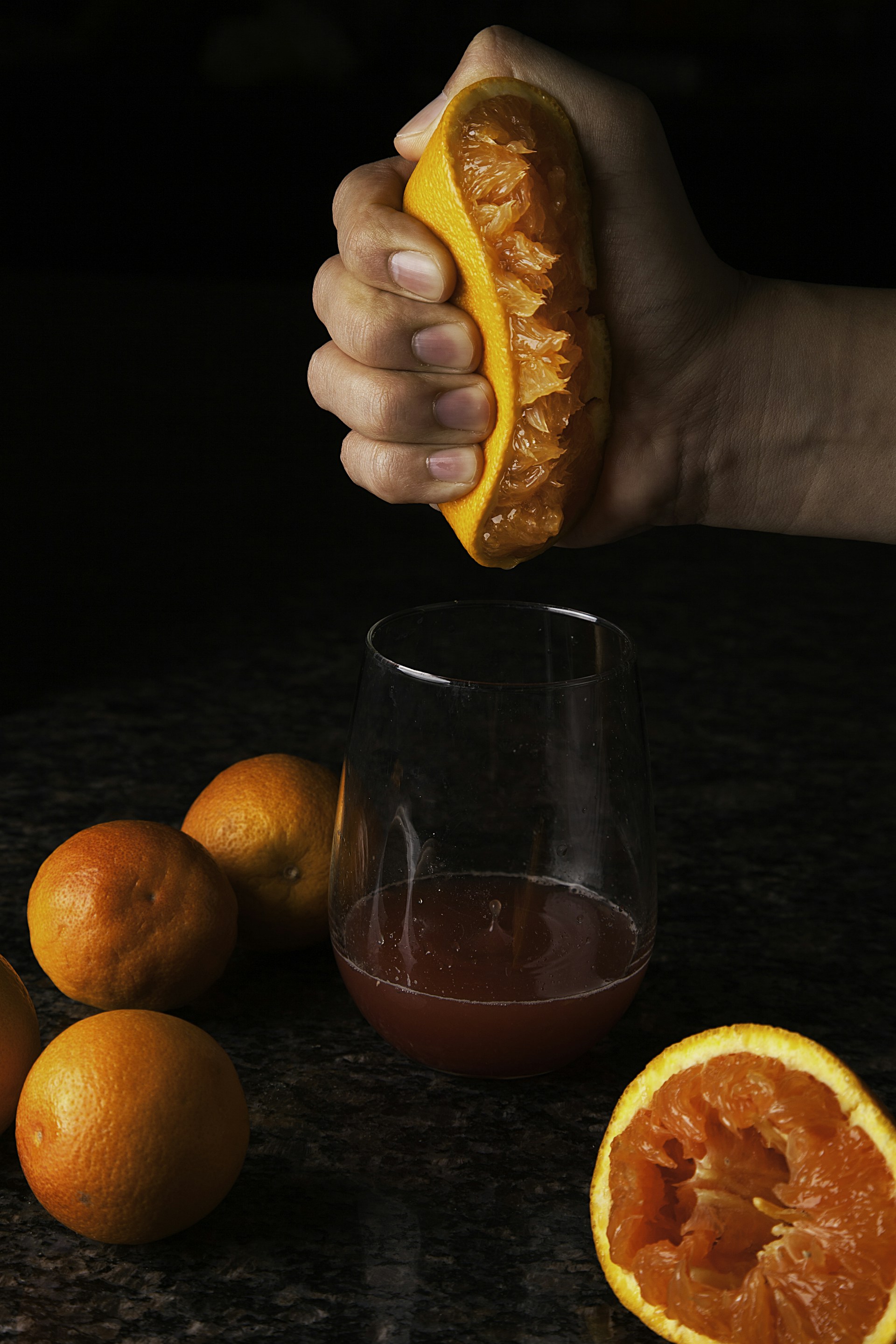 person holding orange fruit beside clear drinking glass with red liquid