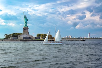 white sail boat on sea near statue of liberty under cloudy sky during daytime