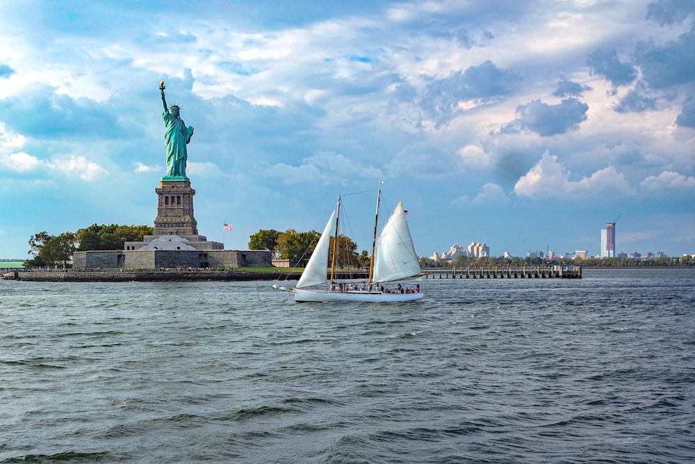 white sail boat on sea near statue of liberty under cloudy sky during daytime