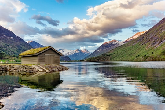 brown wooden house on lake near green mountains under white clouds and blue sky during daytime in Stryn Norway