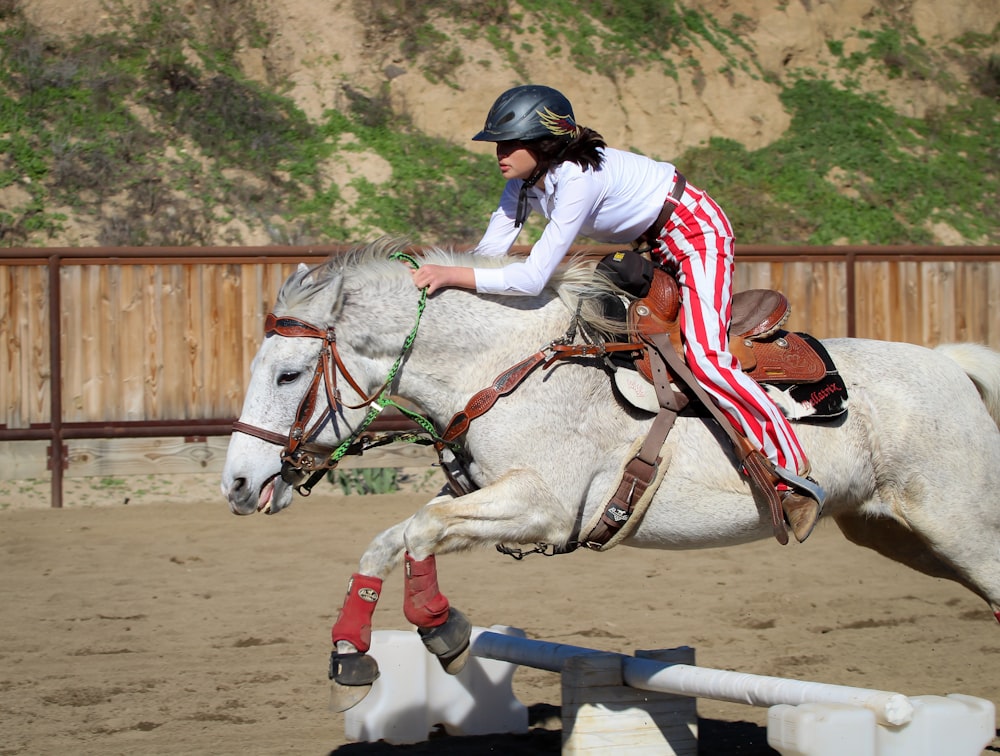 man in white and red long sleeve shirt riding white horse during daytime