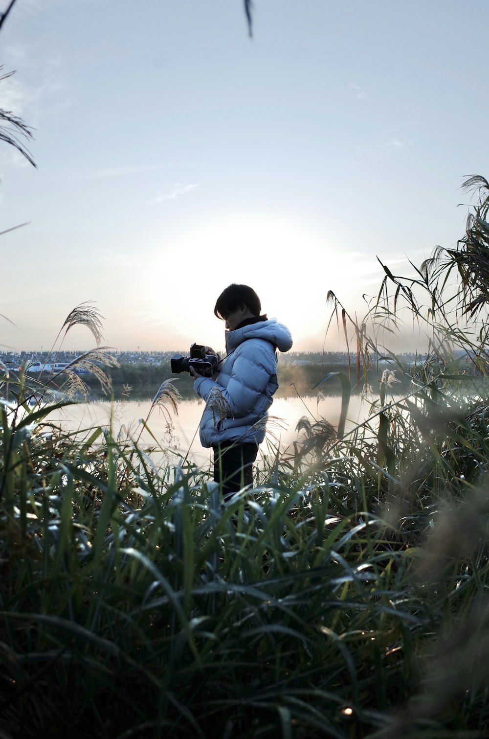 Uomo in giacca blu e pantaloni neri che tiene la fotocamera DSLR nera in piedi sul campo di erba verde