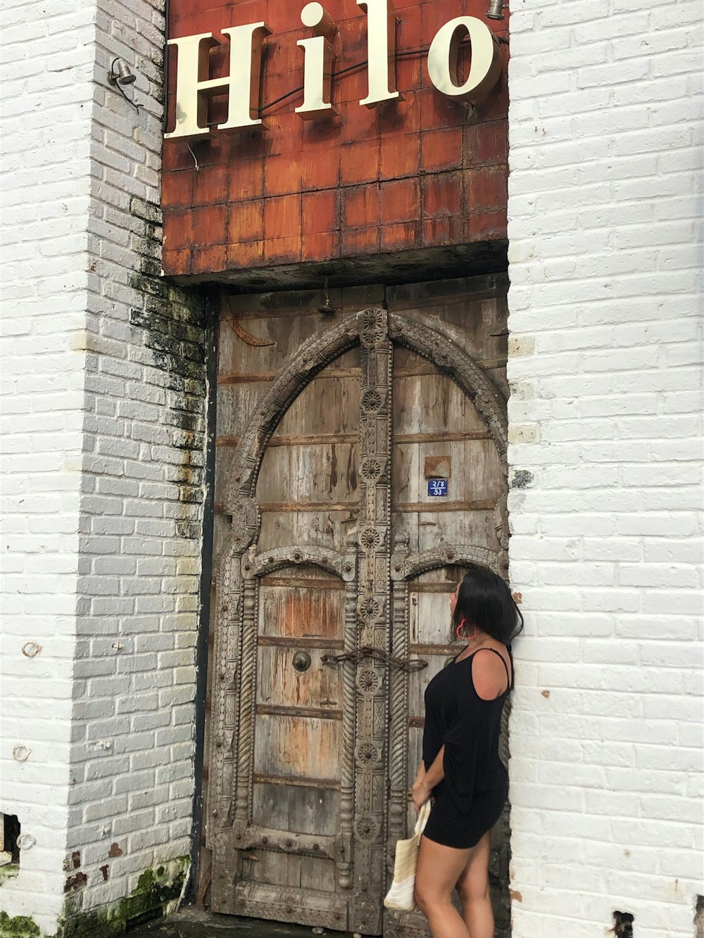 Femme en chemise noire à manches longues debout à côté d’une porte en bois marron