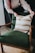 A person is arranging a decorative cushion on a green upholstered armchair. The cushion has a pattern of white and brown stripes. The chair has wooden armrests and is placed on a floor with a light brown rug.