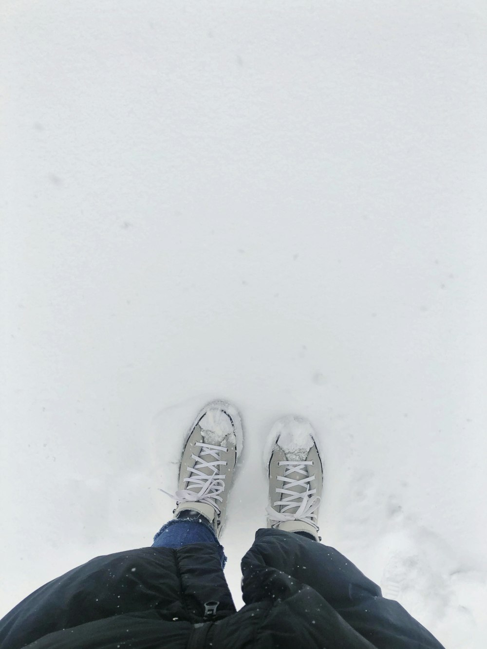 person in blue and white sneakers standing on snow covered ground