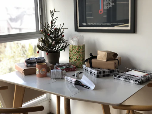 Une table couverte de petits paquets cadeaux emballés, à côté d'un petit sapin