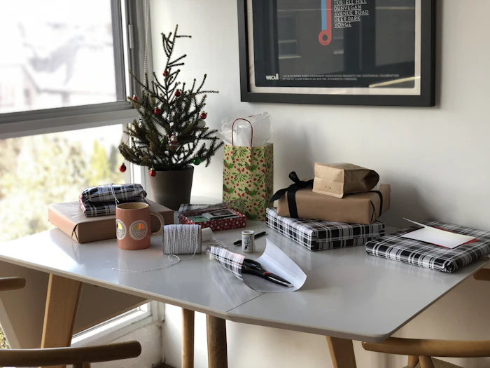 Une table couverte de petits paquets cadeaux emballés, à côté d'un petit sapin