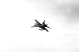 A jet fighter is flying through a cloudy sky, prominently featuring its sleek aerodynamic design against a backdrop of a light, overcast sky.