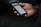 A hand is holding a smartphone with the screen displaying a webpage or app interface, featuring text and images. The background is dark, highlighting the phone.