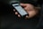 A hand is holding a smartphone with the screen displaying a webpage or app interface, featuring text and images. The background is dark, highlighting the phone.