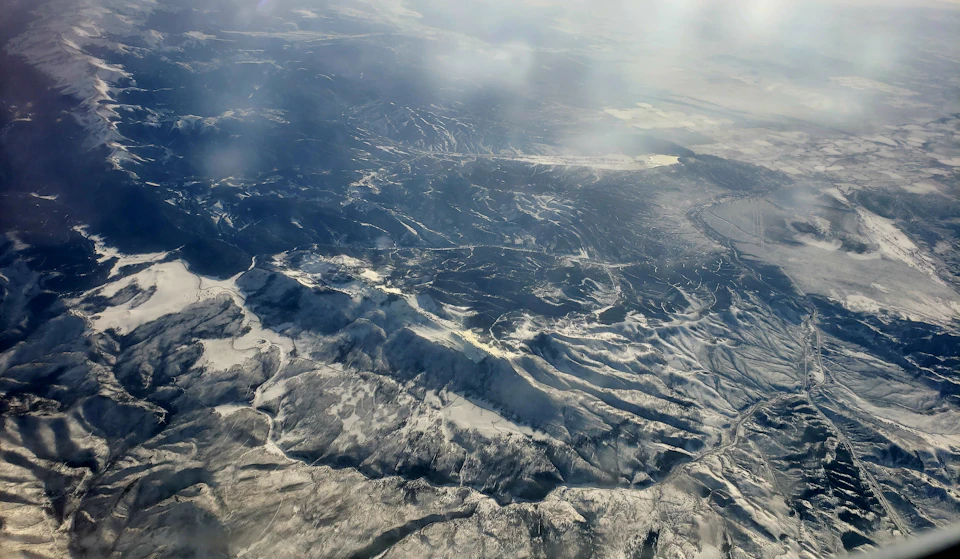 Mountainous landscape with snow-capped peaks and valleys from an airplane window perspective
