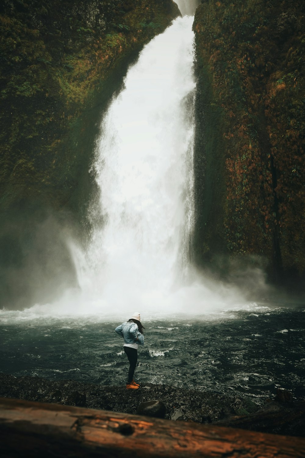 man in blue jacket and blue denim jeans sitting on rock near waterfalls during daytime