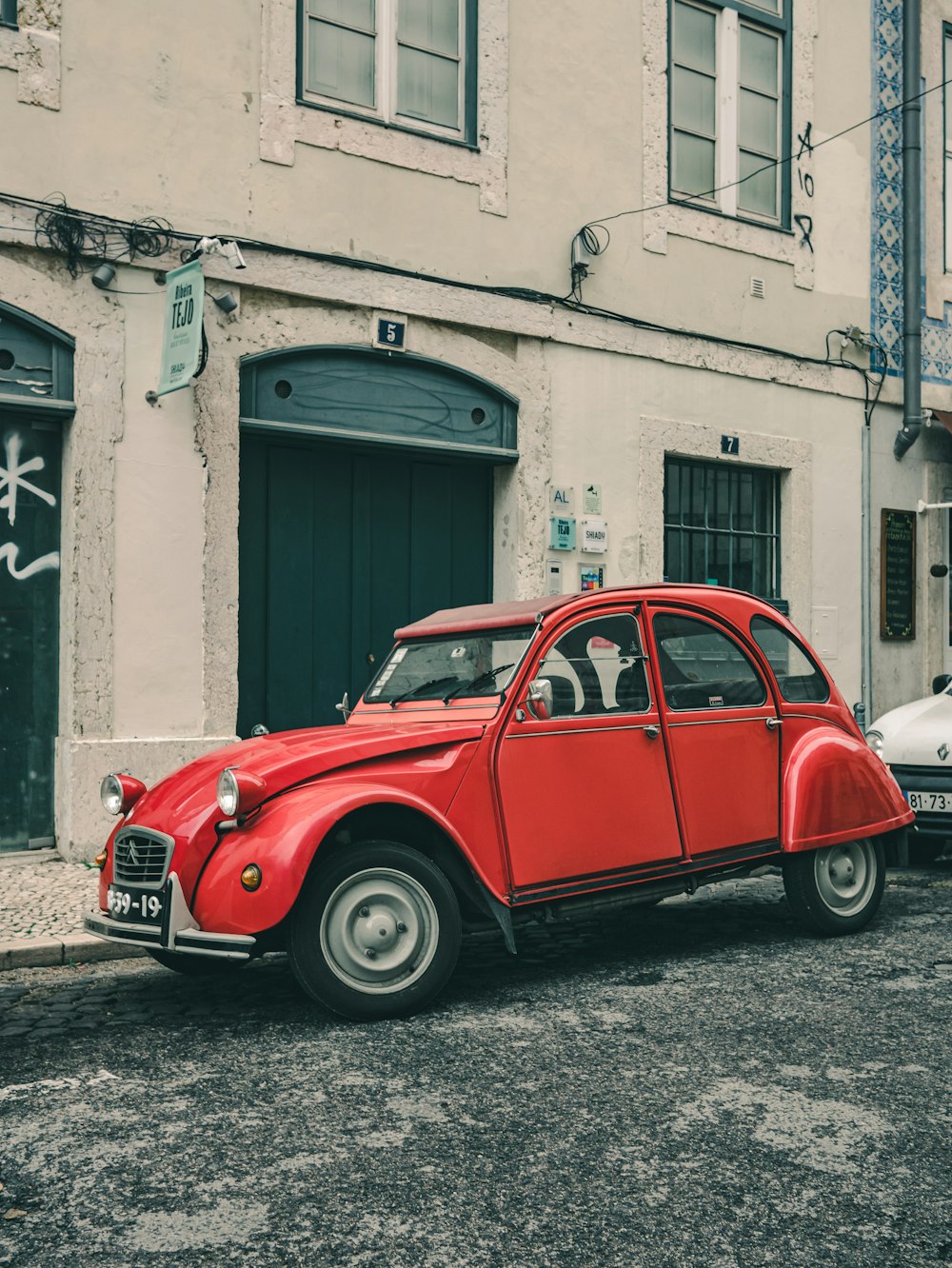 red volkswagen beetle parked beside gray concrete building during daytime
