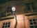 An outdoor street lamp illuminates a residence at night. The light casts warm tones on the walls and balconies, which have ornate iron railings. Blue garlands decorate the area, adding a festive touch. A sign on one of the balconies reads 'STA. MARIA MAIOR'.