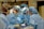 Several surgeons, dressed in blue surgical gowns and protective masks, are performing a medical procedure in an operating room. Surgical instruments, such as scalpels and forceps, are visible in the foreground. The environment is clinical and filled with medical equipment.