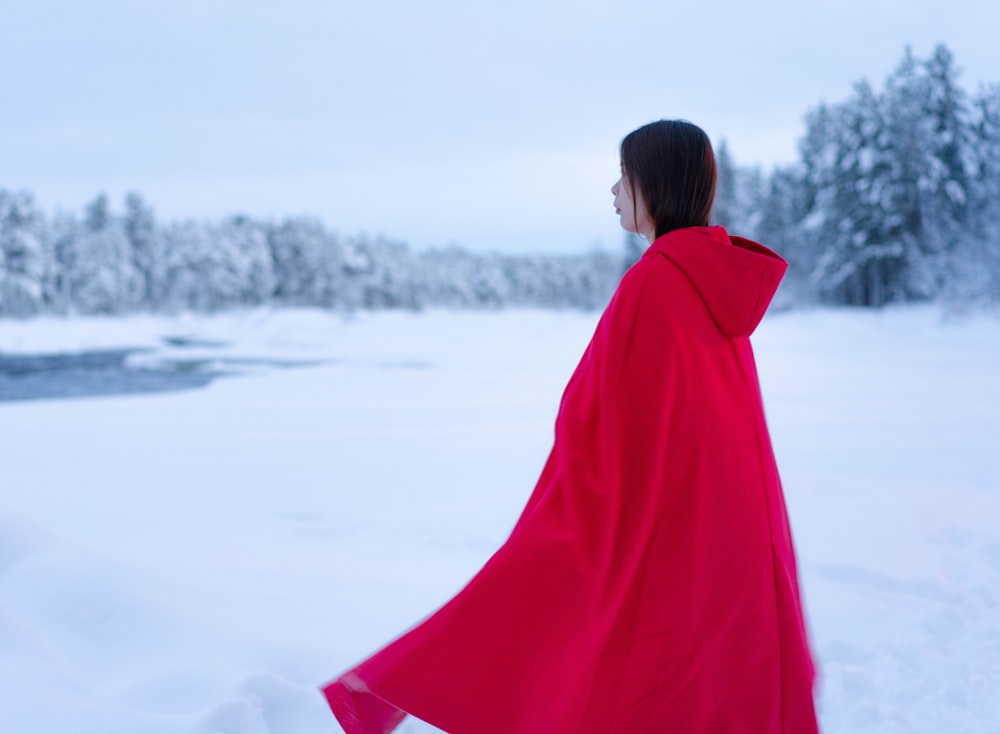 昼間、雪に覆われた地面に立つ赤いコートの女性