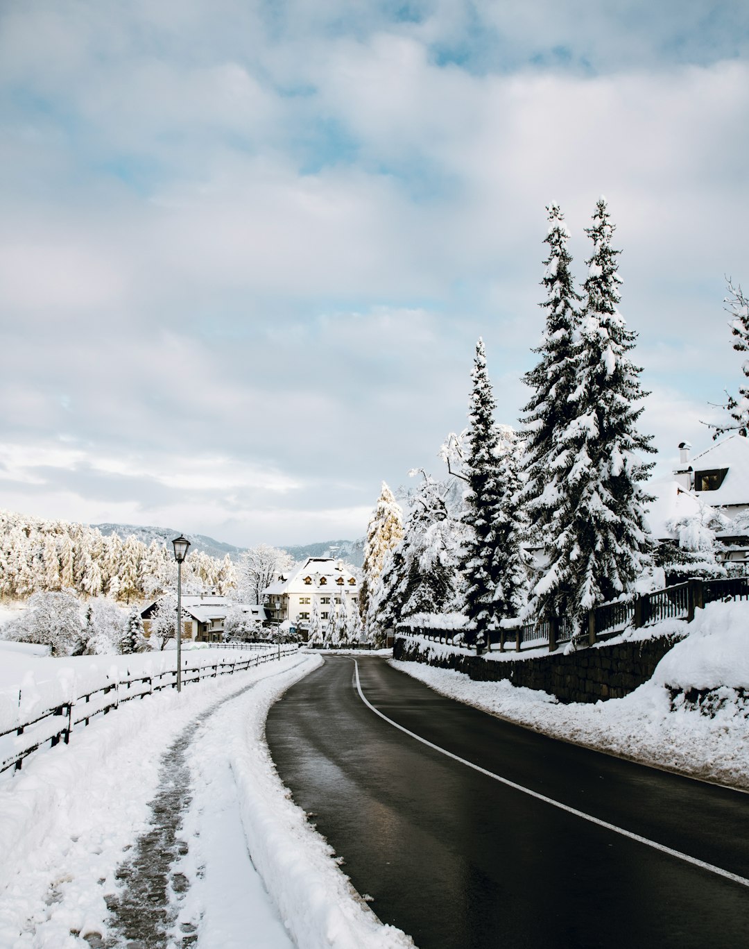 snow covered road near trees and houses under white clouds and blue sky during daytime