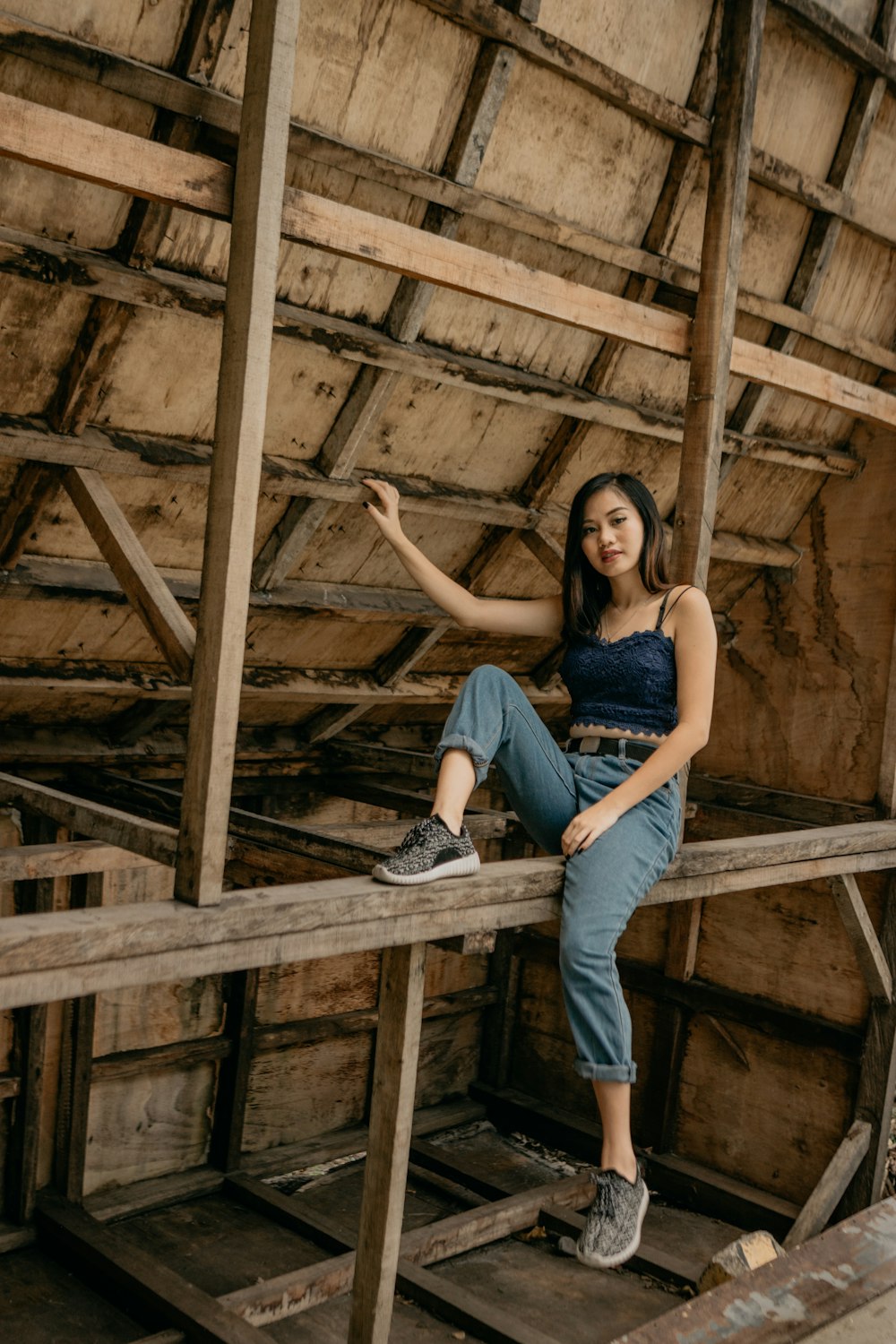 woman in blue denim jeans and black tank top sitting on brown wooden frame
