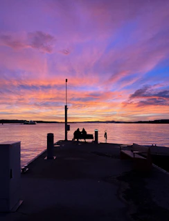 A serene sunset view with silhouettes of two people sitting together on a bench.