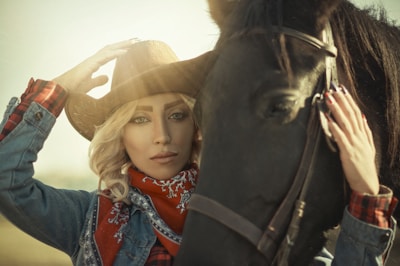 woman in blue denim jacket wearing brown cowboy hat beside black horse during daytime